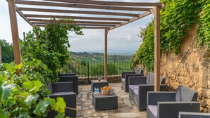 A covered outdoor seating area with wicker furniture and a stone floor, overlooking a scenic landscape.