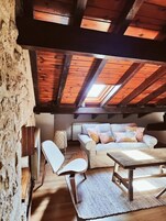 Um loft aconchegante com vigas de madeira aparentes, um sofá branco com almofadas coloridas, uma cadeira branca e uma mesa de madeira.