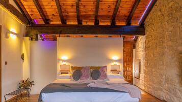 Un dormitorio con techo de madera, paredes de piedra, una cama con almohada floral, lámparas de noche y un banco con flores.