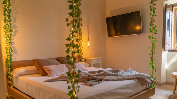 A neatly made bed with a white comforter and pillows, a bedside table with a lamp, and a wall-mounted TV.
