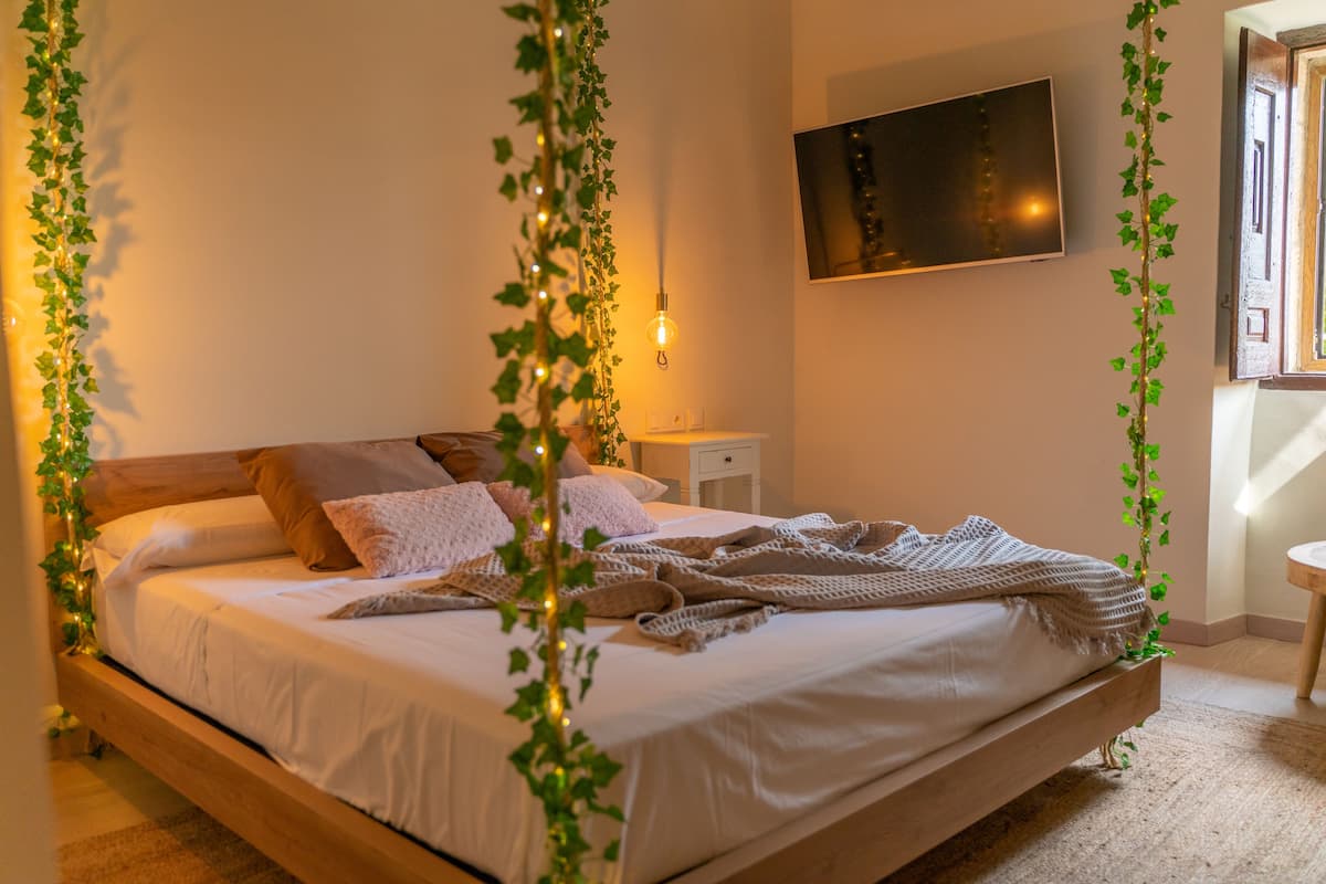 A neatly made bed with a white comforter and pillows, a bedside table with a lamp, and a wall-mounted TV.