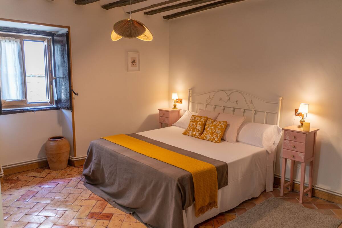 A bedroom with a bed, bedside tables, a window, and a hanging light fixture.