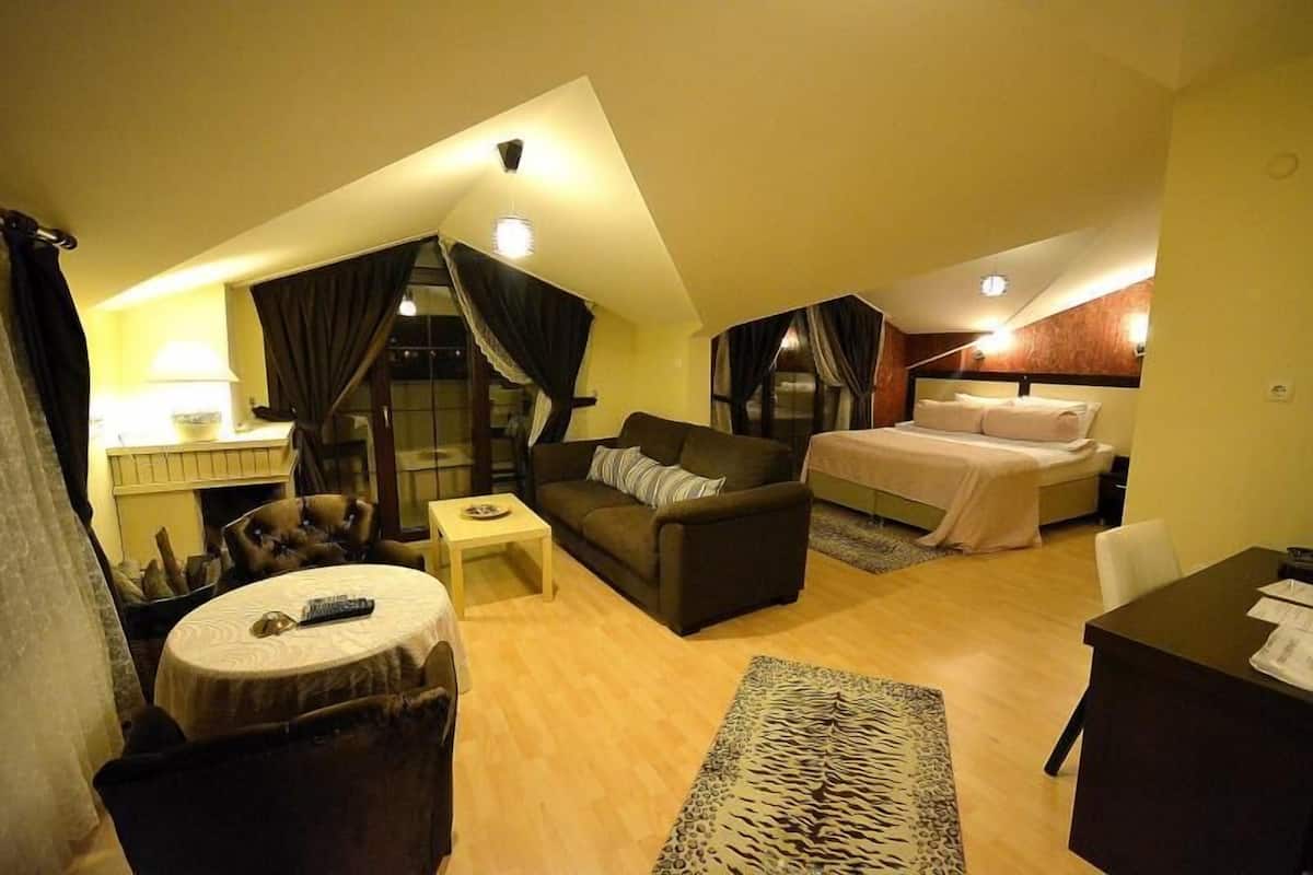 A compact, well-lit room with a bed, a sofa, a small table, and a chair.