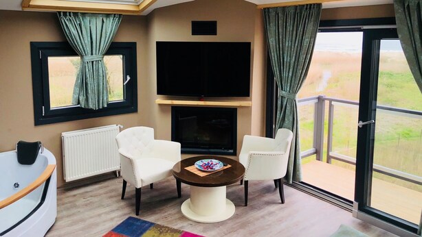 A modern living room with a flat-screen TV, two white armchairs, a round coffee table, and a skylight. - Velena Hotel (Sile)