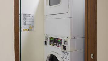 A compact laundry room with a stacked washer and dryer, a control panel, and a ventilation system on the ceiling.