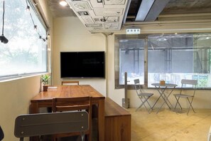 Una habitación con una mesa y sillas de madera, un televisor de pantalla plana y ventanas grandes.