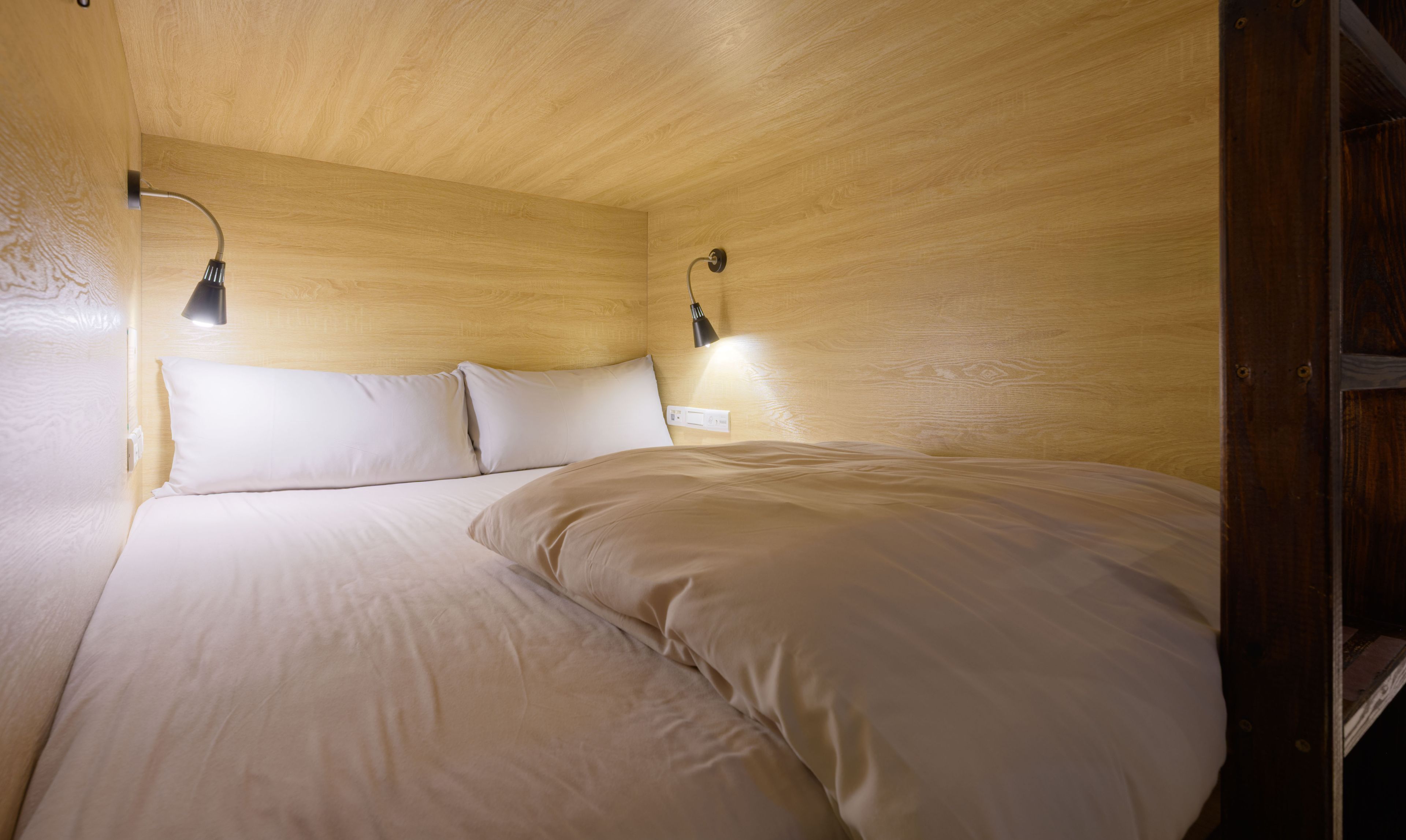 A wooden-paneled room with a bed, two wall-mounted lamps, and a visible electrical outlet.