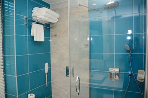 A modern bathroom with blue tiles, a glass shower enclosure, a towel rack with white towels, a handheld showerhead, and a built-in toilet.