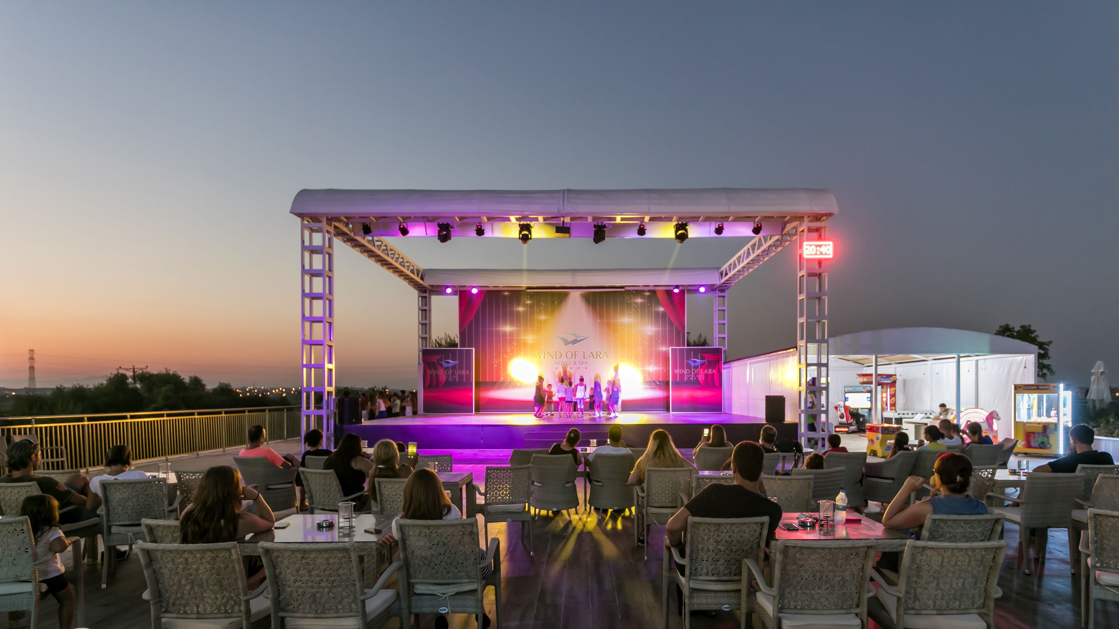 An outdoor stage with a performance, surrounded by dining tables and chairs.