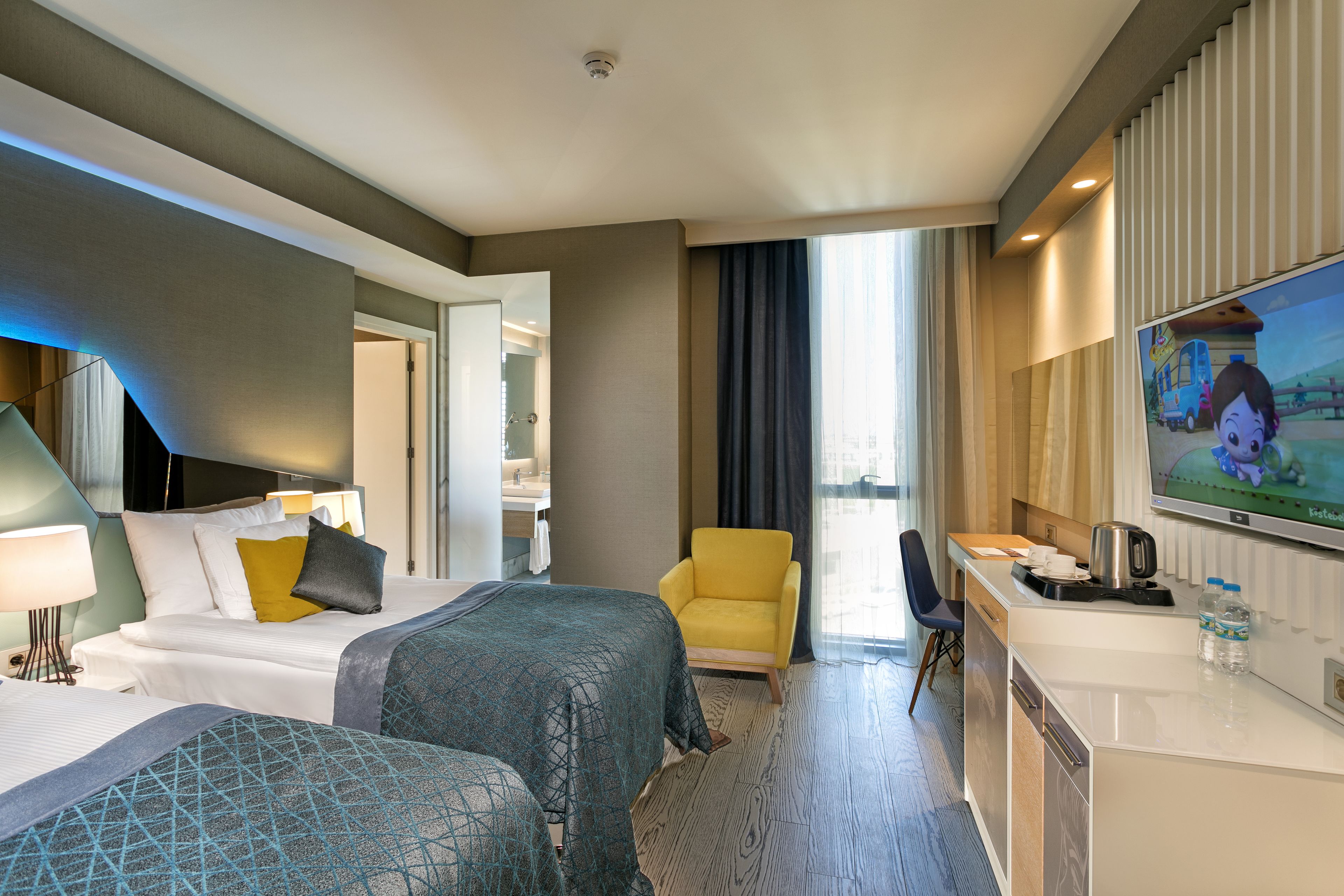 A hotel room with two beds, a desk with a coffee maker, a TV, and a view of the city.