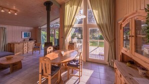 L’intérieur d’un chalet en bois comprend une table à manger, des chaises, un canapé, un téléviseur et une grande fenêtre avec des rideaux.
