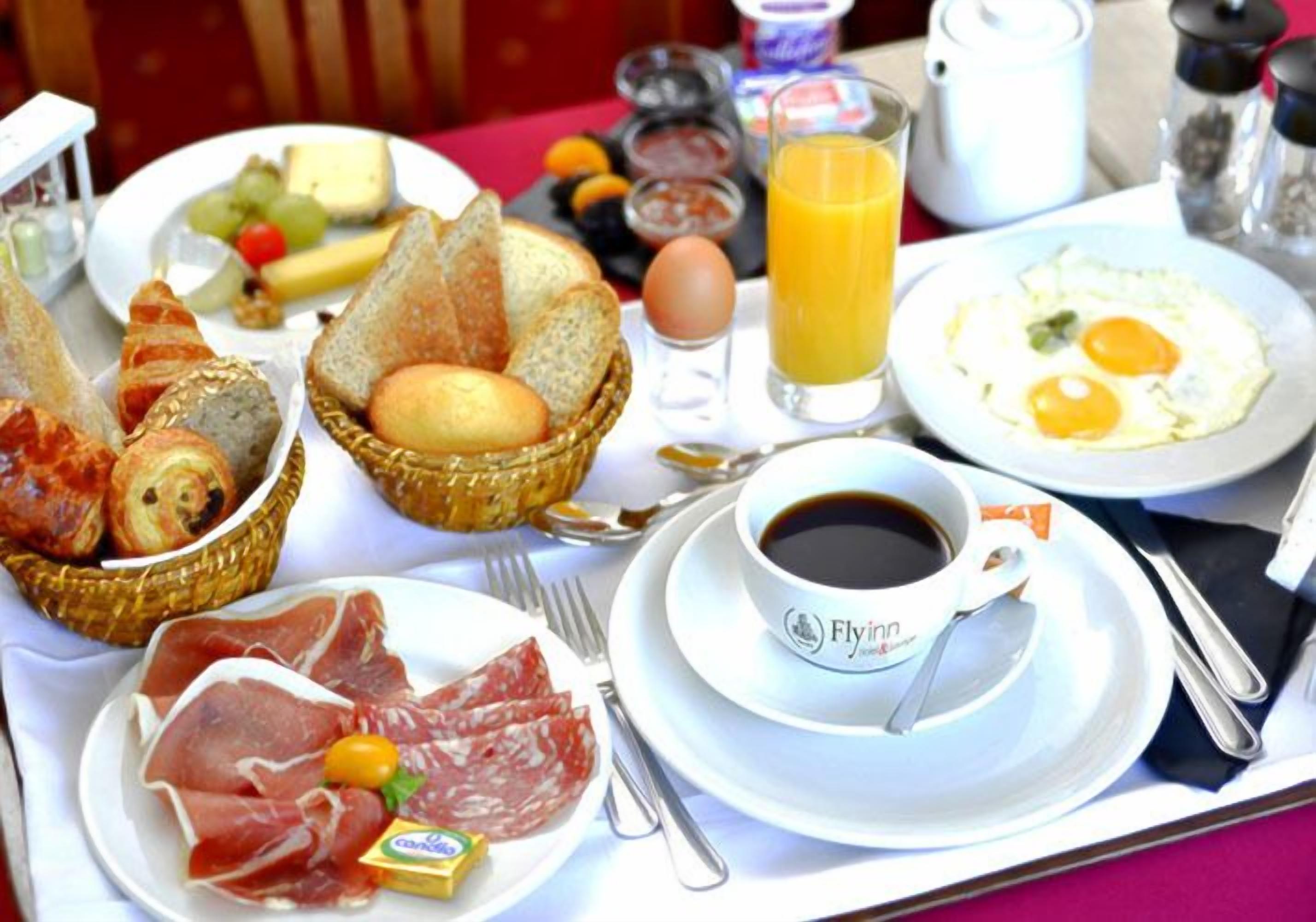 A breakfast tray with various foods including bread, eggs, cheese, and meats, along with a cup of coffee and a glass of orange juice.