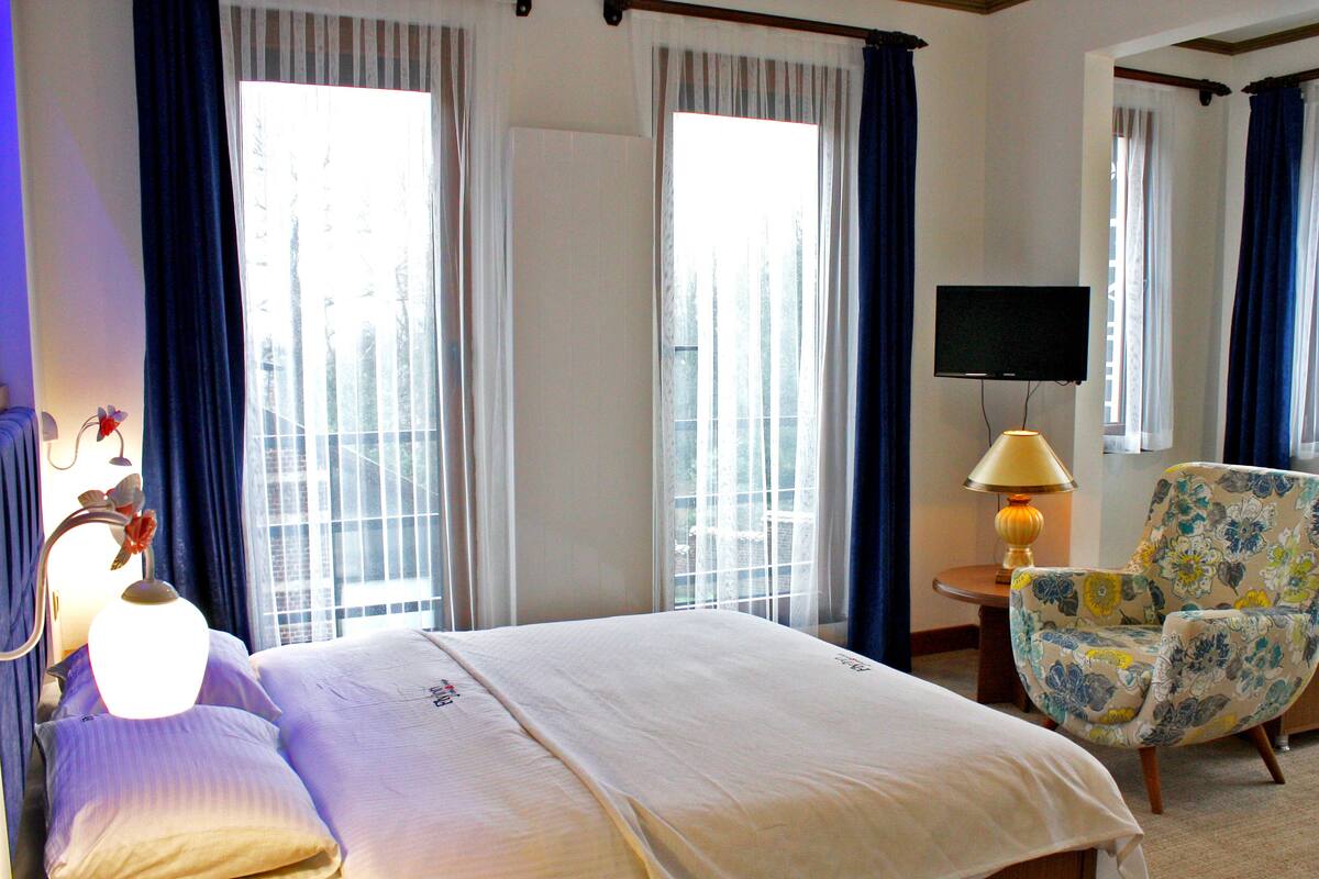 A hotel room with a bed, a chair, a lamp, and a TV.