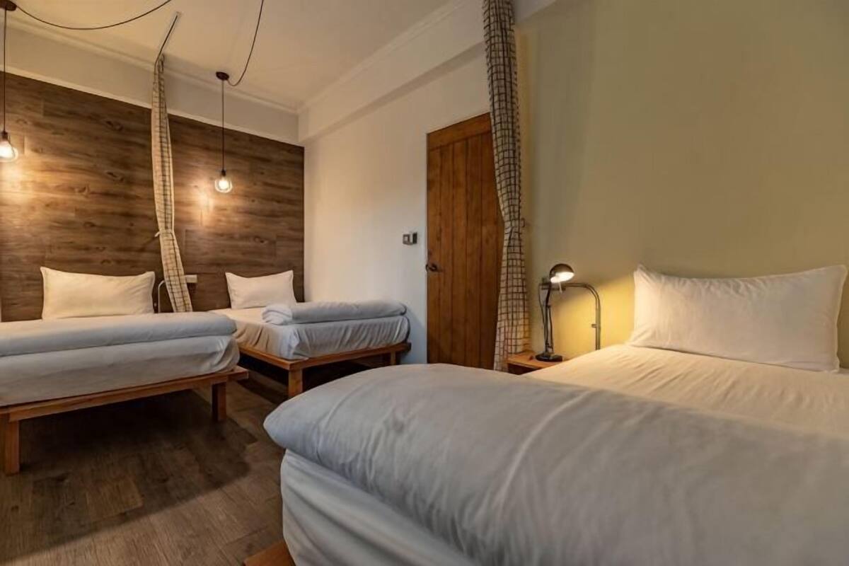 Een kamer met drie bedden, een houten hoofdbord en een houten deur.