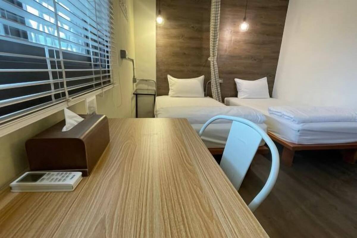 Een hotelkamer met een houten tafel, twee bedden, een bureau en een raam met zonwering.
