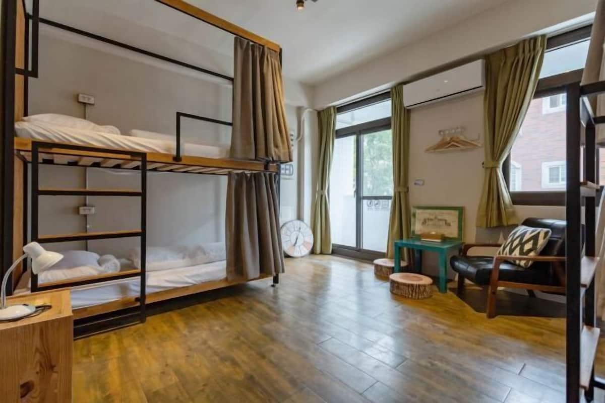 Een slaapkamer met een stapelbed, een houten bureau, een stoel, een klein tafeltje en een klok.