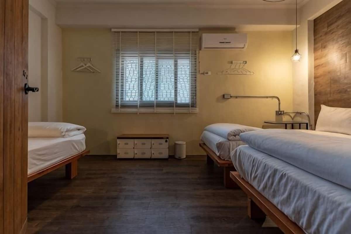 Un dormitorio con dos camas, una ventana con persianas, una mesita de noche con lámpara y un armario.