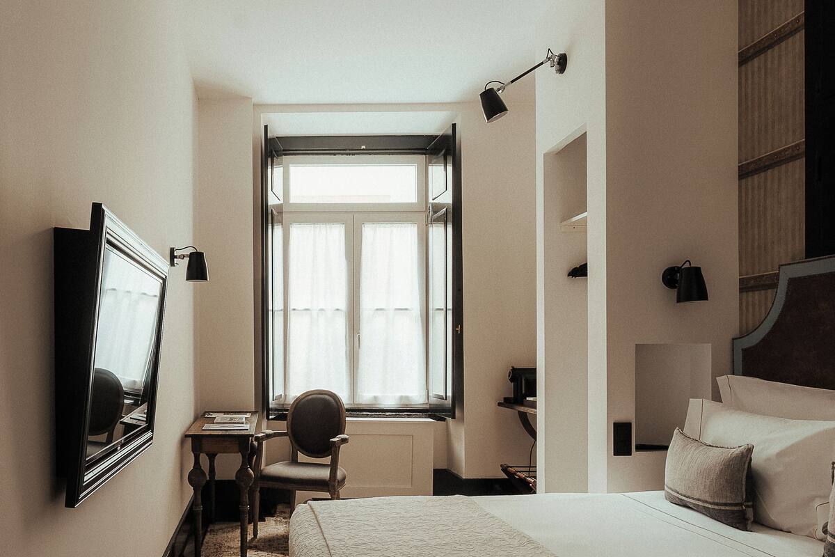 A hotel room with a bed, a desk, a chair, a TV, and a window.