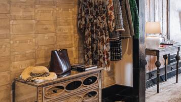 A room with a rustic brick wall, a wooden dresser with drawers, a hat on the dresser, and a coat rack with various garments.