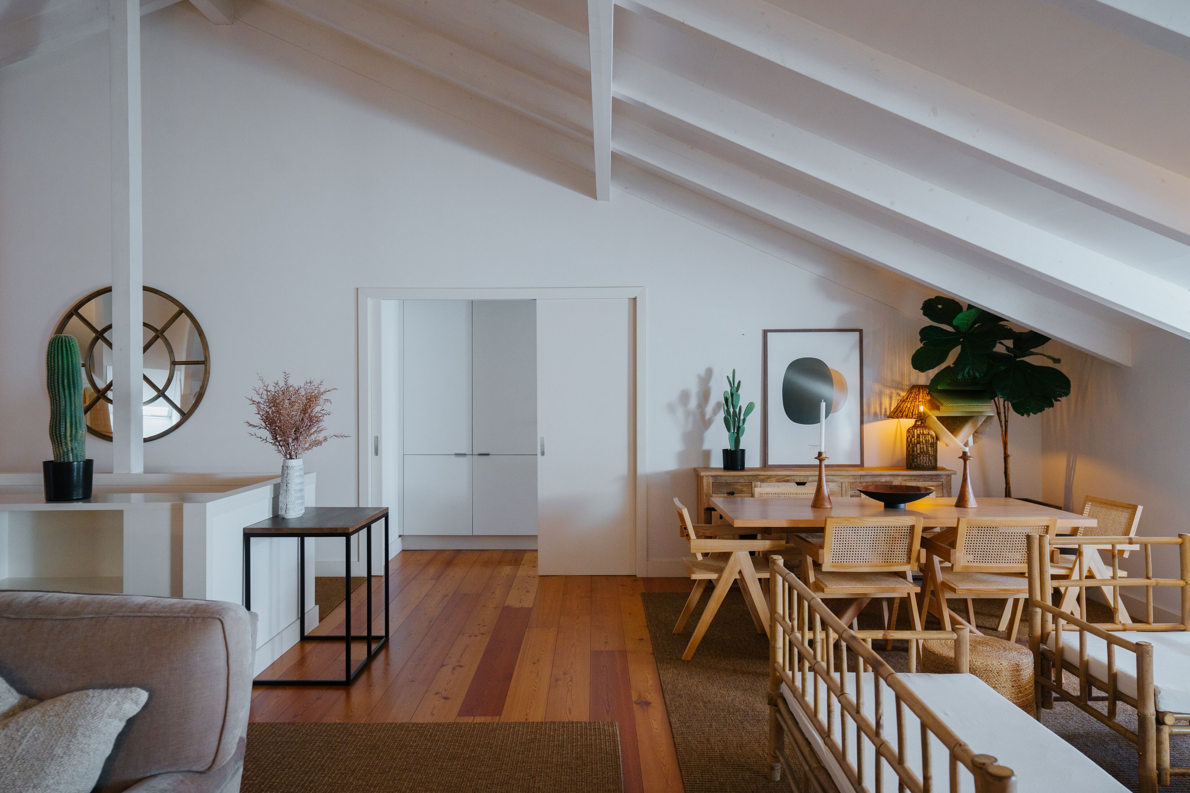 A modern living space with a wooden floor, a dining area with a table and chairs, a sofa, and a white door leading to another room.