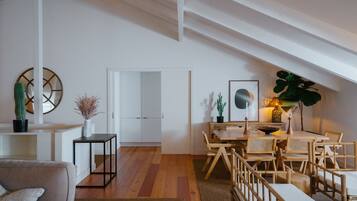 A modern living space with a wooden floor, a dining area with a table and chairs, a sofa, and a white door leading to another room.