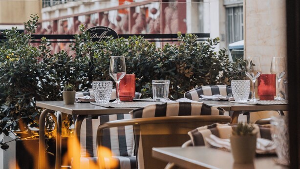 Un café al aire libre con mesas y sillas, una fogata al frente y un edificio con balcones al fondo.