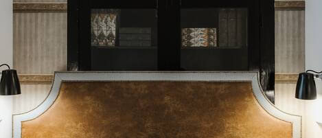 A bed with a headboard, two bedside lamps, and a window with a view of boxes.