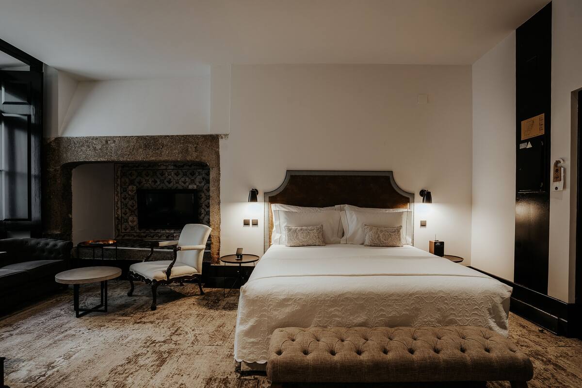 A bedroom with a large bed, a fireplace, a seating area with a table and chairs, and a television.