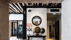 Un vestíbulo con suelo de piedra, una mesa negra con objetos decorativos y un espejo montado en la pared.