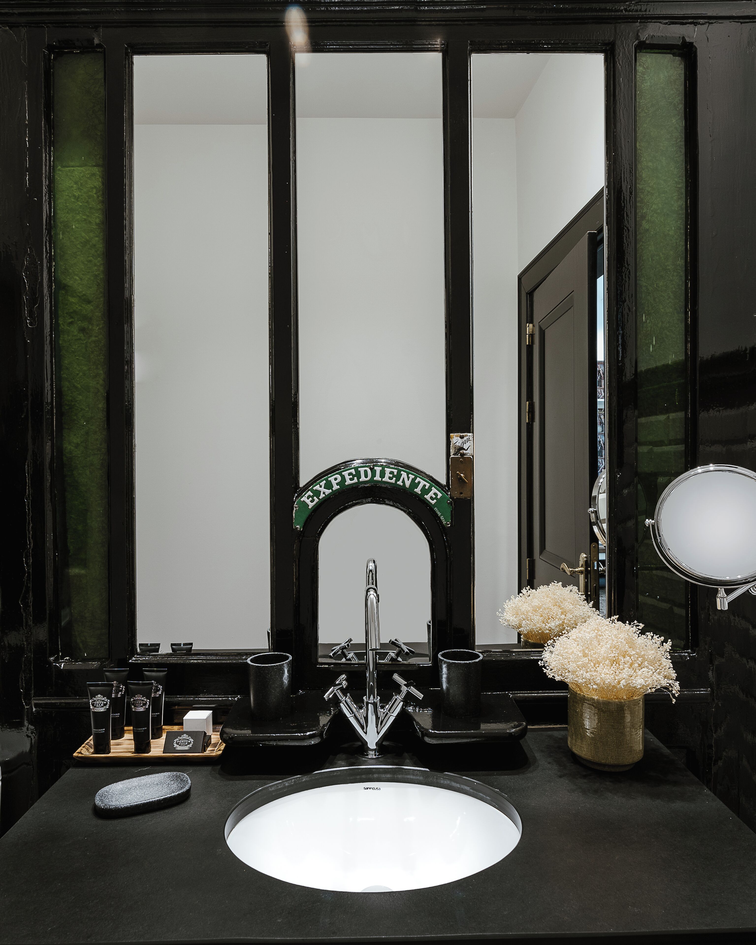 Un baño con lavamanos negro, espejo y un cartel verde sobre el espejo.