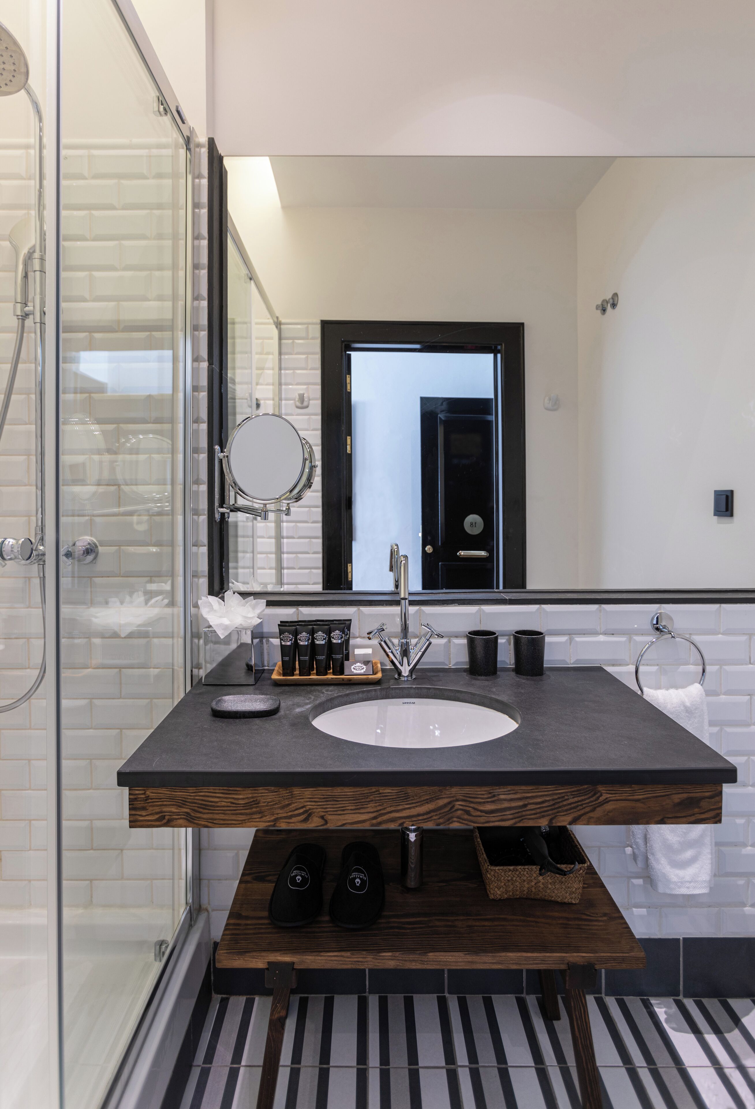 Un baño moderno con cabina de ducha de vidrio, un espejo grande, tocador de madera y piso a rayas blanco y negro.