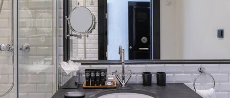 Un baño moderno con cabina de ducha de vidrio, un espejo grande, tocador de madera y piso a rayas blanco y negro.