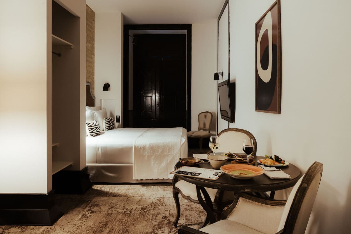 A hotel room with a bed, a dining table with plates and glasses, a chair, and a mirror.