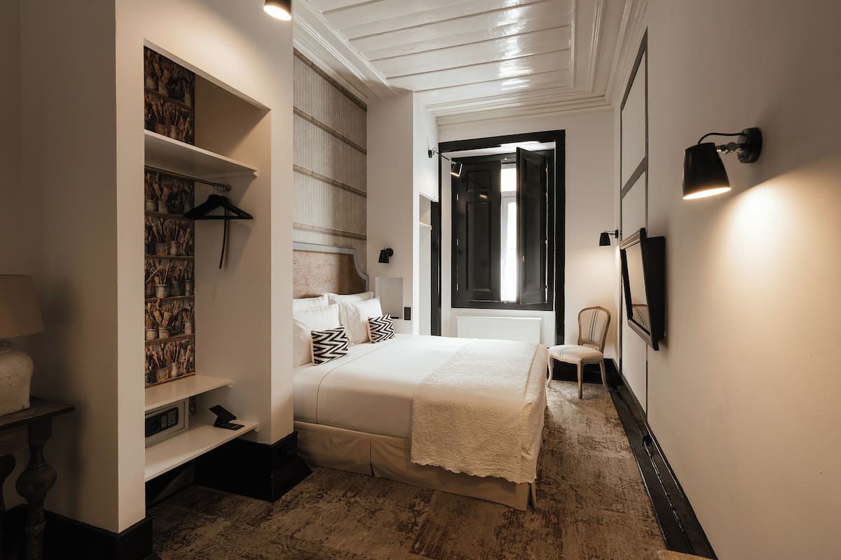A bedroom with a bed, a wardrobe, a chair, and a door leading to another room.