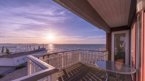 A balcony with a glass table and a view of the sea at sunset. - Ferienpark Mueritz (Rechlin)