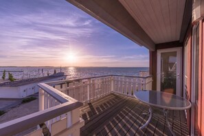 A balcony with a glass table and a view of the sea at sunset. - Ferienpark Mueritz (Rechlin)
