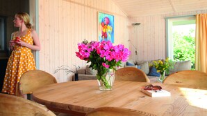 A wooden interior with a round wooden table, a vase of pink flowers, and a woman in a polka dot dress. - Ferienpark Mueritz (Rechlin)