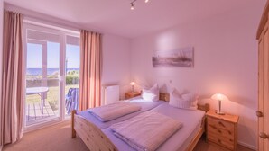 A bedroom with a large bed, two bedside tables, a nightstand, a view through a sliding glass door to an outdoor area, and a painting on the wall. - Ferienpark Mueritz (Rechlin)