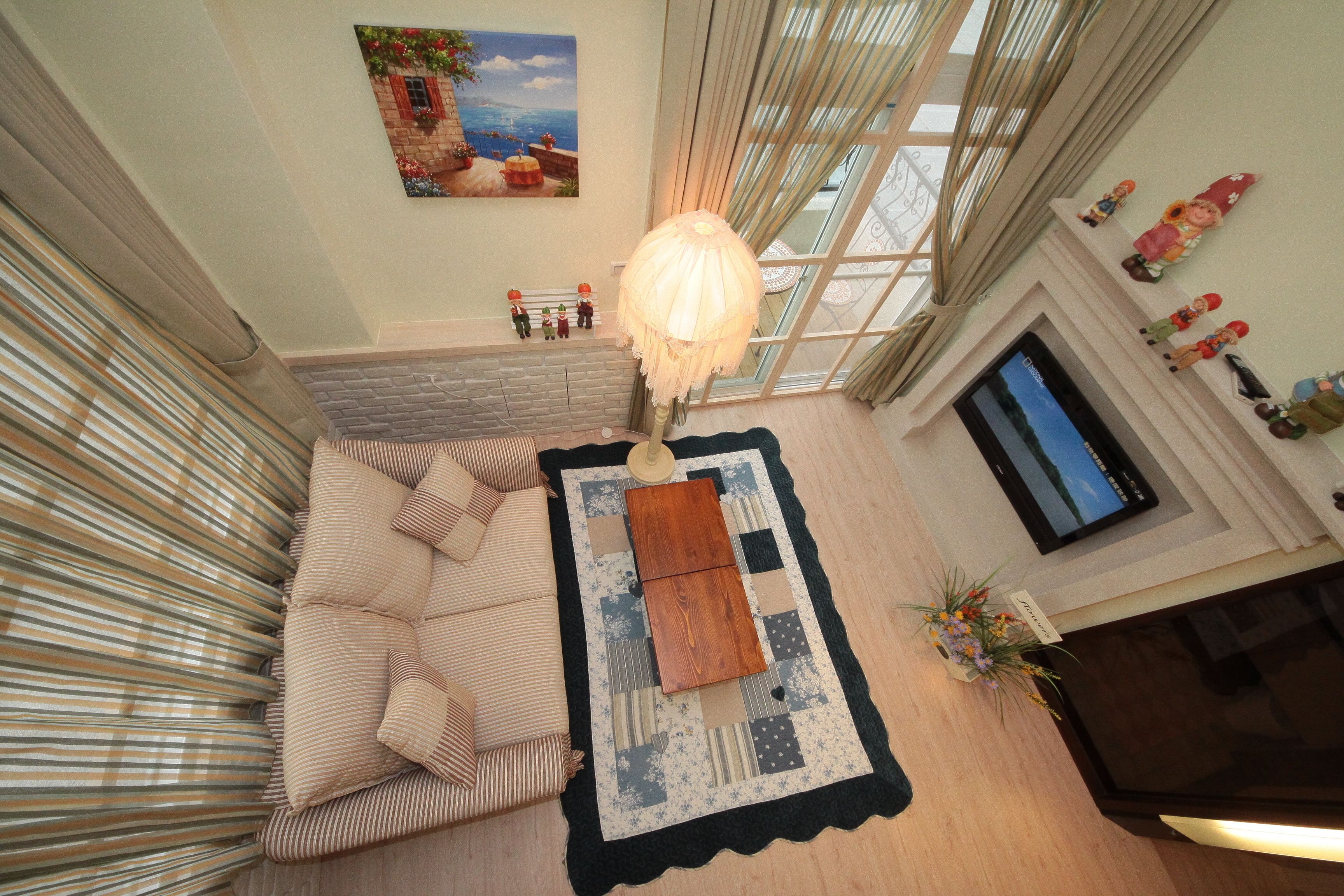 A cozy living room with a sofa, a coffee table, and a TV. There is a window with curtains and a painting on the wall.