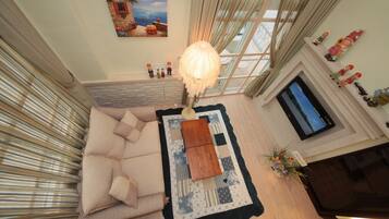 A cozy living room with a sofa, a coffee table, and a TV. There is a window with curtains and a painting on the wall.