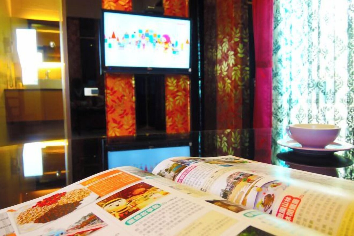 A hotel room with a television on the wall, a magazine on the table, and a bowl on a stand.