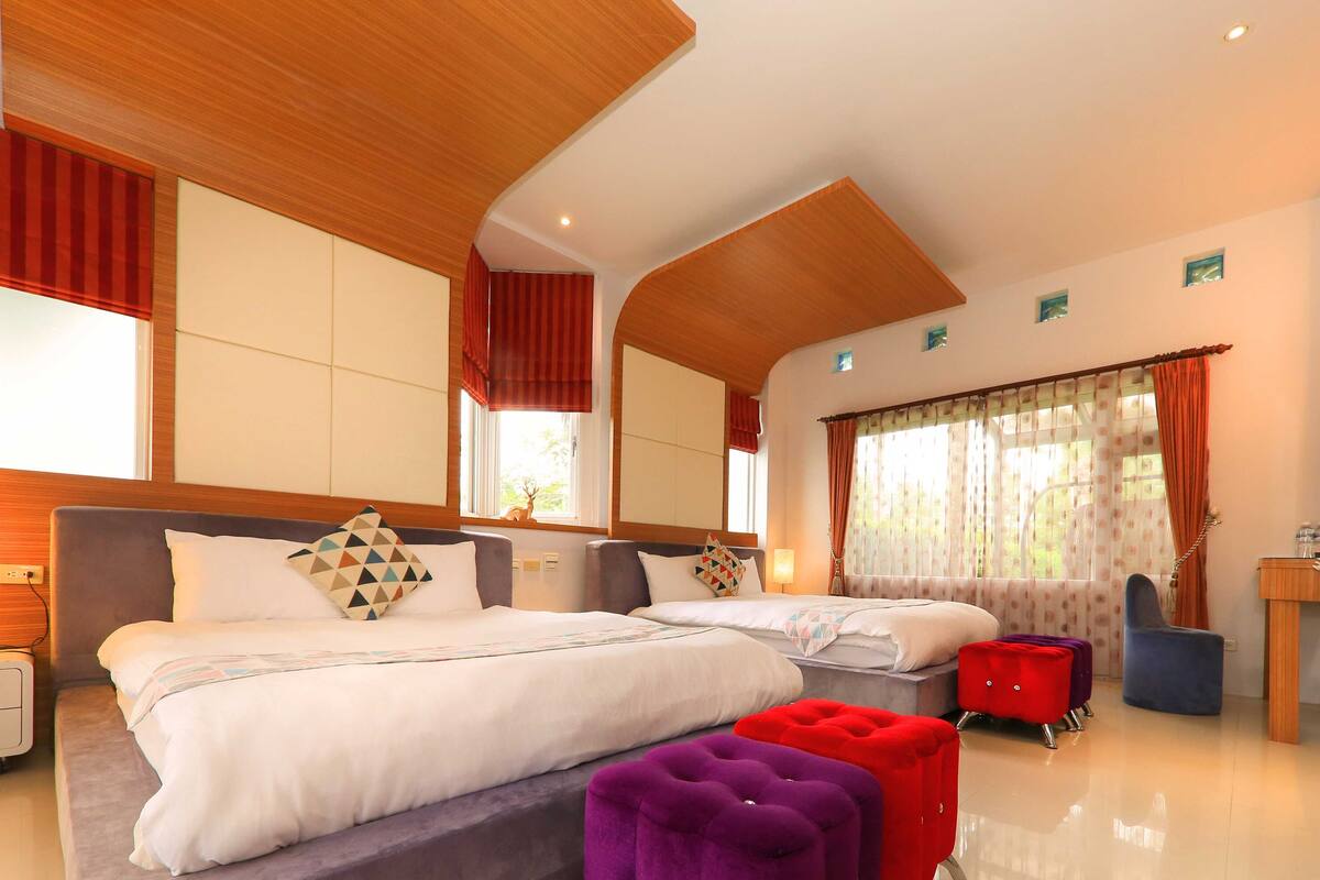 A modern hotel room with a large bed, a smaller bed, a desk, and a bathroom.