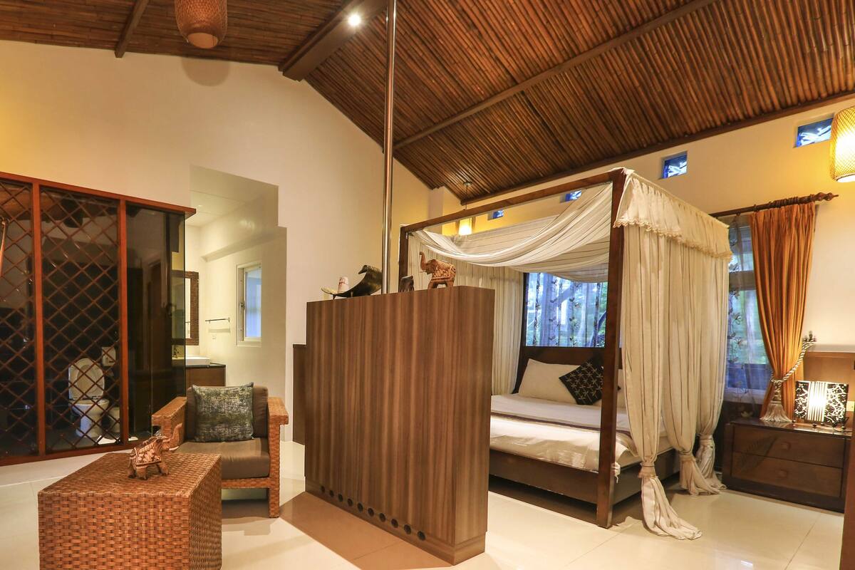 A room with a bed, a sofa, a wicker chair, and a wooden partition.