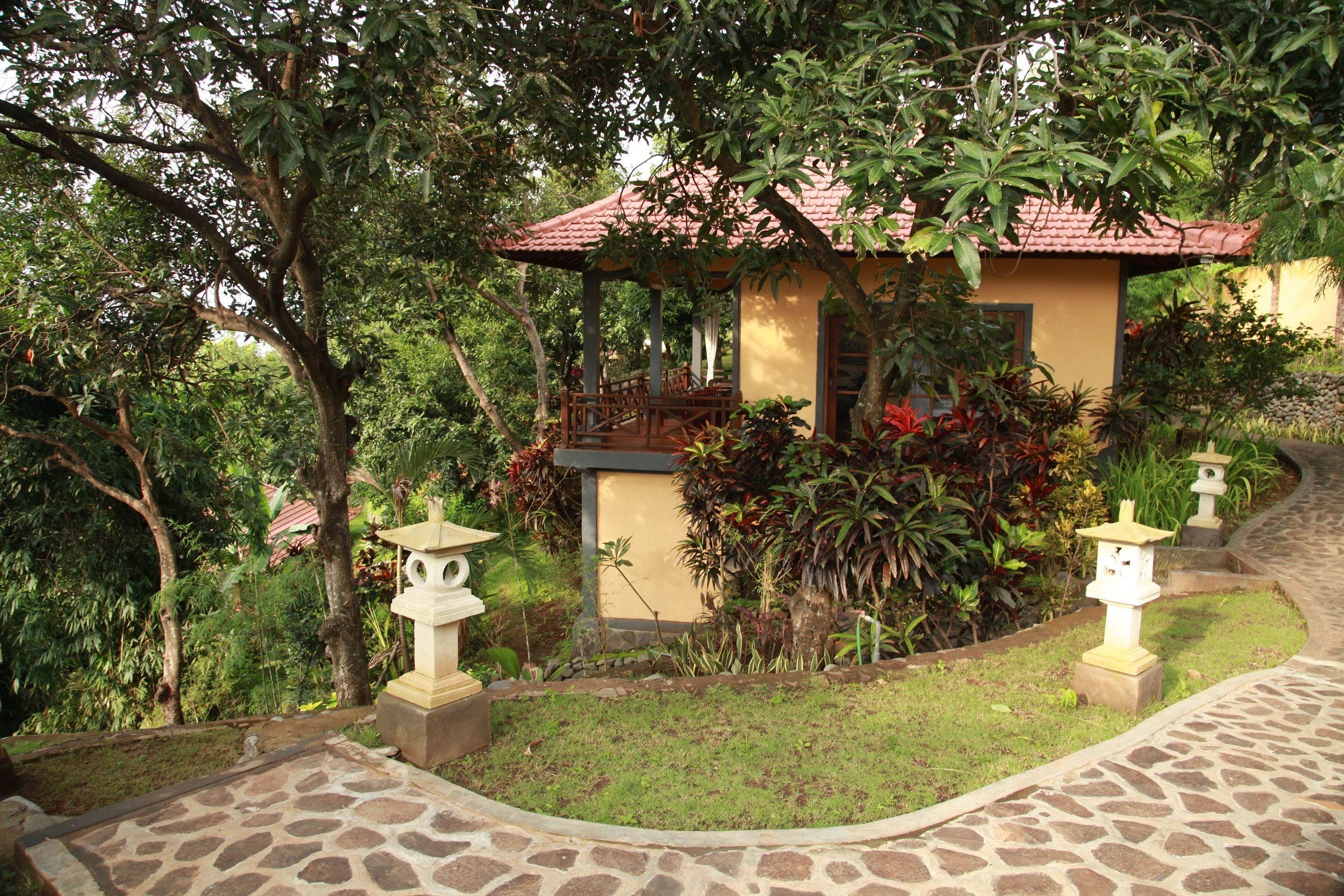 A small building with a red-tiled roof, surrounded by lush greenery and stone pathways.