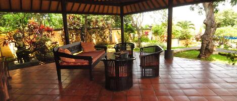 A covered patio with tiled flooring, a sofa, two chairs, and a small table.
