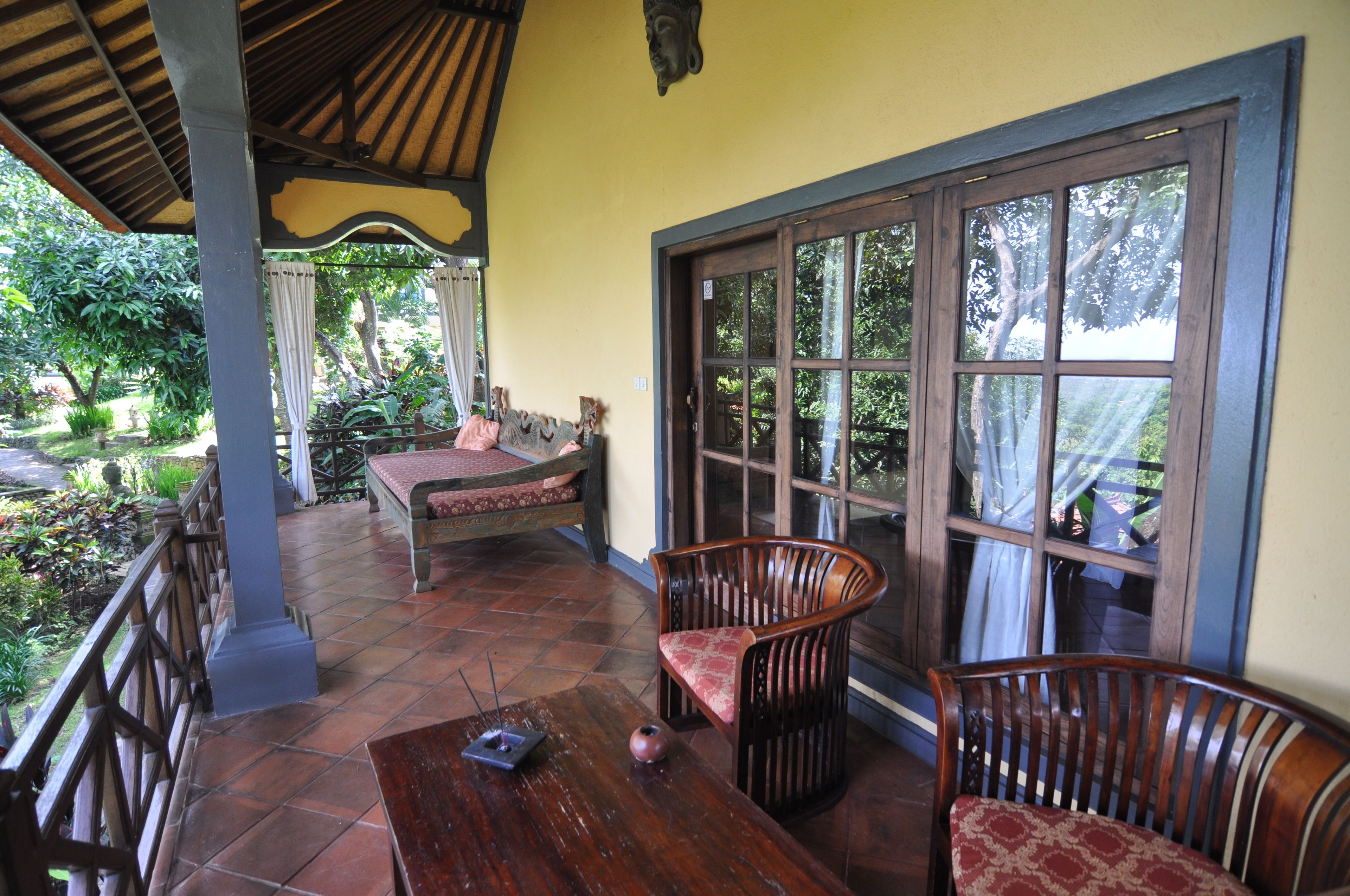 A covered patio area with a wooden table, two chairs, a bench, and a large window.