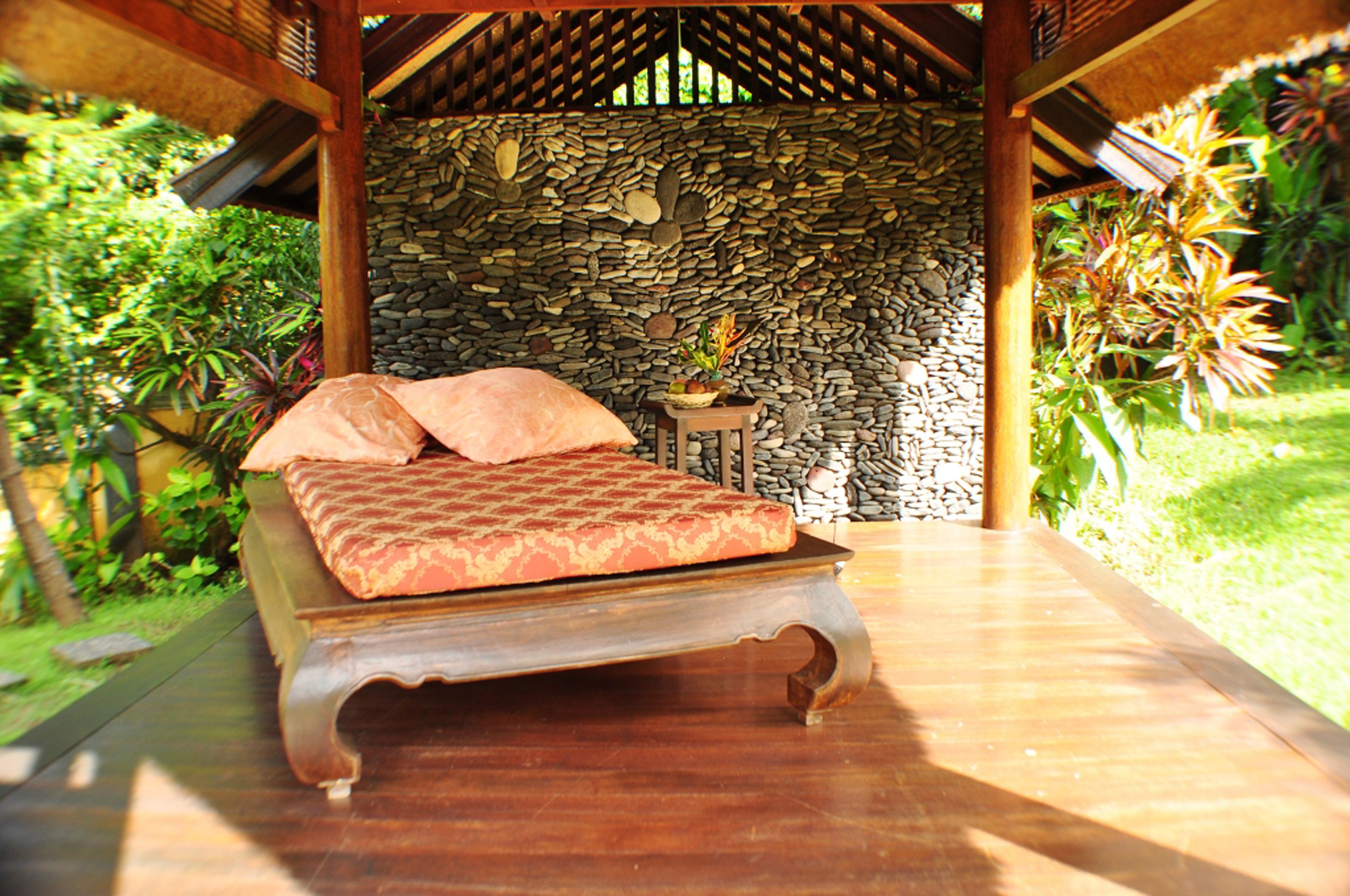A bed with a patterned bedspread and pillows, a stone wall, and a small table with a plant.