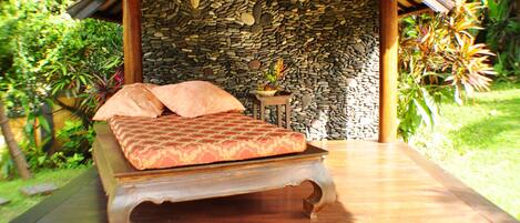 A bed with a patterned bedspread and pillows, a stone wall, and a small table with a plant.