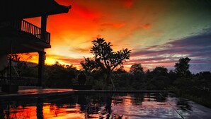 Ein Sonnenuntergang über einem Gewässer, im Vordergrund ein Gebäude und Bäume.