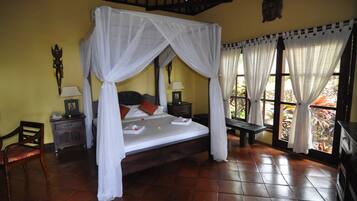 A four-poster bed with white drapes, a wooden nightstand with a lamp, a chair, and a bench.